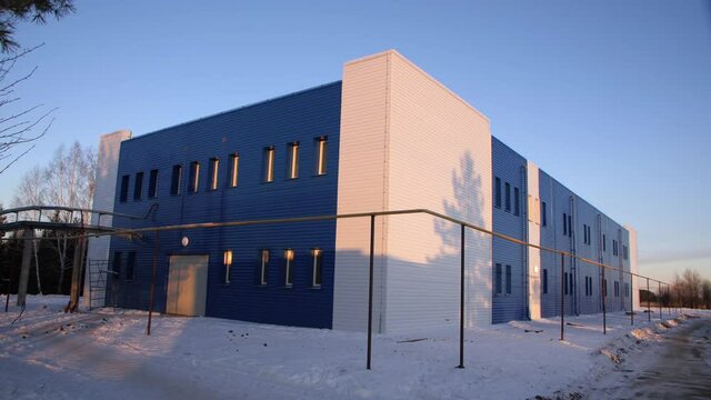 Contemporary blue and white workshop building surrounded by outside gas pipeline under clear sky at sunset in winter evening