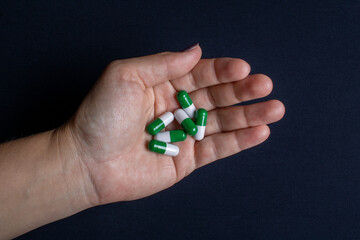 White woman's hand with green and white medicine capsules used to improve cellulite and sagging skin. Mainly used by the female audience in search of an aesthetic improvement.