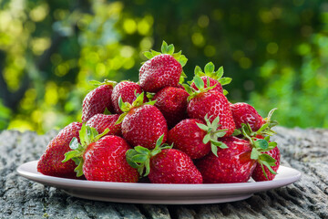 Fresh ripe strawberries in a plate on a wooden table in the garden