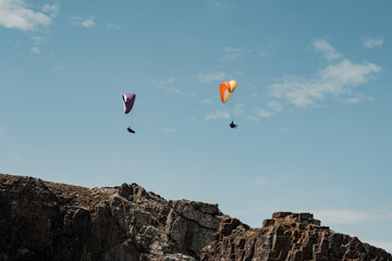 Horizontal shot of two paragliders gliding over a cliff.