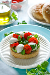 Caprese  open faced sandwich with cherry tomatoes, mini mozzarella cheese and basil leaves drizzled with olive oil served on a white plate, close up.