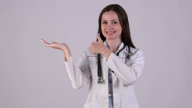 Young Female Doctor in medical Uniform pointing index finger aside on empty palm showing thumb up like. Medical workers showing advertising area for commercial text, copy space on hand.