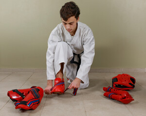 Caucasian teenager putting on taekwondo foot guard. Safety clothing for martial arts and combat sports.
