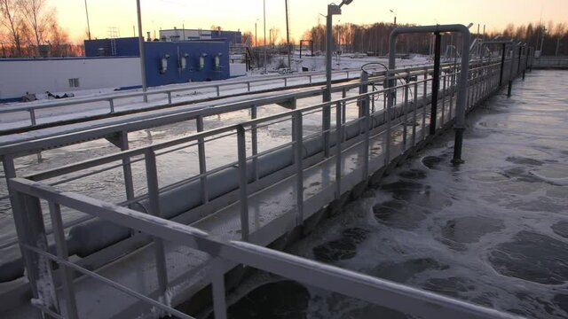 Large pools with purified wastewater and empty metal bridge at contemporary treatment plant at sunset light close view