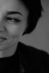 A happy young girl in a black leather jacket and short hair is sitting at a table. Black and white portrait of a smiling woman	