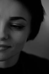 Fototapeta premium A happy young girl in a black leather jacket and short hair is sitting at a table. Black and white portrait of a smiling woman 