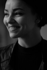 A happy young girl in a black leather jacket and short hair is sitting at a table. Black and white portrait of a smiling woman	