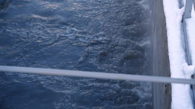 Swirling purified wastewater in large reservoir and snowy ground at contemporary treatment plant extreme close view
