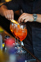 three glasses of cocktails on the bar. bartender pours a glass of sparkling wine with Aperol.
