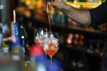 three glasses of cocktails on the bar. bartender pours a glass of sparkling wine with Aperol.