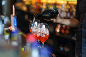 three glasses of cocktails on the bar. bartender pours a glass of sparkling wine with Aperol.