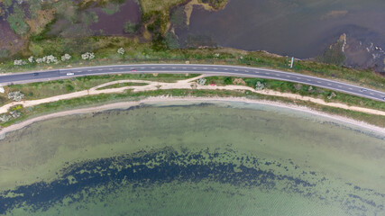 A highway that runs along a narrow spit between the sea and the estuary. Cars on the road. Aerial view.