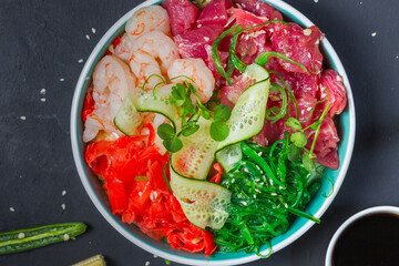 Poke, a Hawaiian dish. Diced tuna, shrimp, chuka lettuce, and pickled ginger. Top view, close-up on a black background