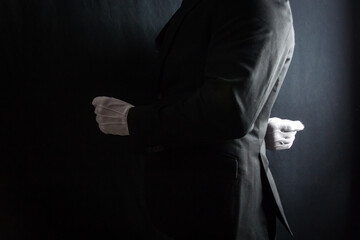 Portrait of Butler or Servant in Dark Suit and White Gloves Standing at Exquisite Attention on Black Background. Service Industry and Professional Hospitality.