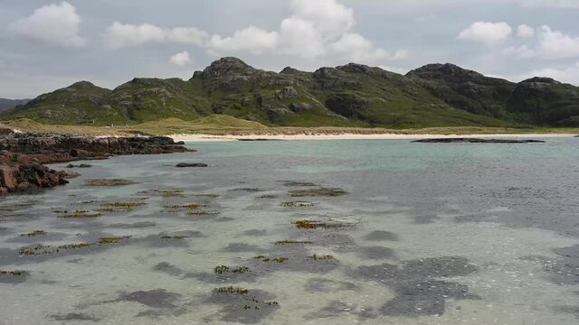 4k real time footage of gentle water movement at Sanna Bay, Ardnamurchan, Scotland on a sunny day. White sand beach and green hills in background.