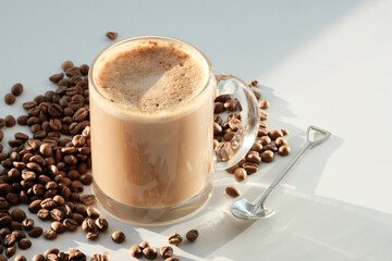 Cappuccino in a glass transparent large glass next to the coffee beans. Gray background.