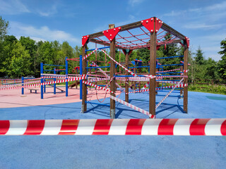 Closed outdoor child playground in sunny day in city park in Moscow, Russia. No children. Barricade tapes hangs on playground. Selective focus. Illness prevention theme.