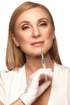 Portrait of a beautiful elderly woman in a white shirt with classic makeup and blond hair with syringe in hands