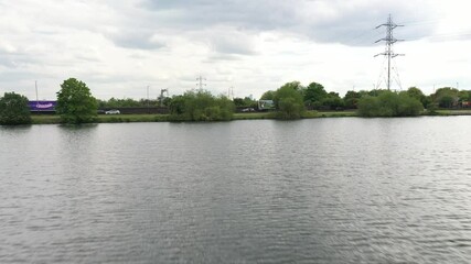 Backwards low flight above rippled water level in industrial landscape with high voltage power lines