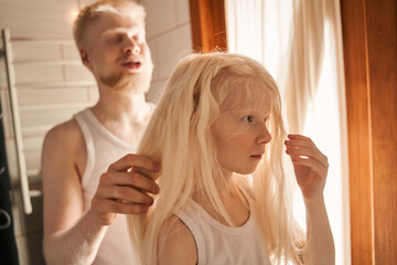 Fototapeta premium Girl standing at the bathroom and waiting while her father making braids for her