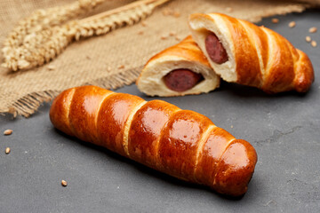 Rolled hot dog sausages in the dough baked in puff pastry on dark background