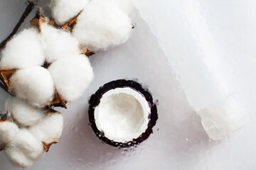 moisturizing skin care. Face and hand cream with cotton flower under a glass surface with water on white background