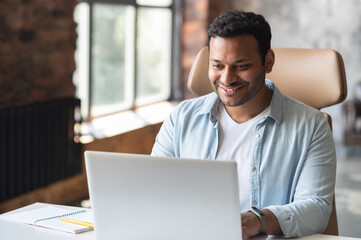 Intelligent indian businessman using a laptop in the office. Smart smiling man entrepreneur looks...