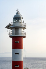 Fototapeta na wymiar Lighthouse in sunset time on the ocean and blue sky background