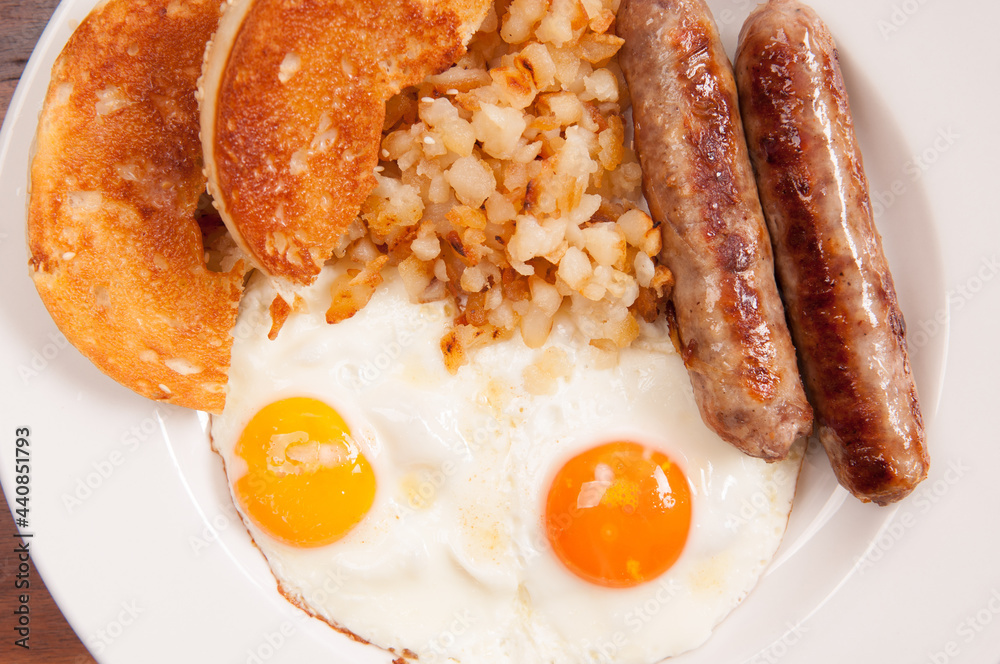 Sticker closeup shot of eggs with different colored yolks, sausage, and bagel on a white plate