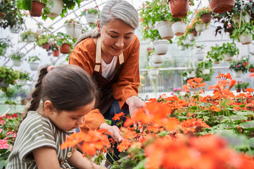 Child helping to her elderly grandmother at the greenhouse in summer outside - obrazy, fototapety, plakaty