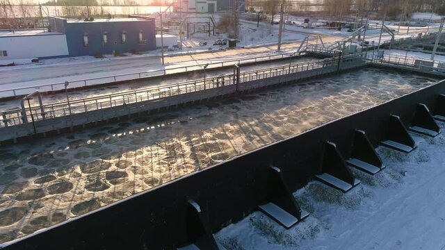 Wastewater undergoes aeration process in large basin at contemporary filtration station in early winter morning aerial view