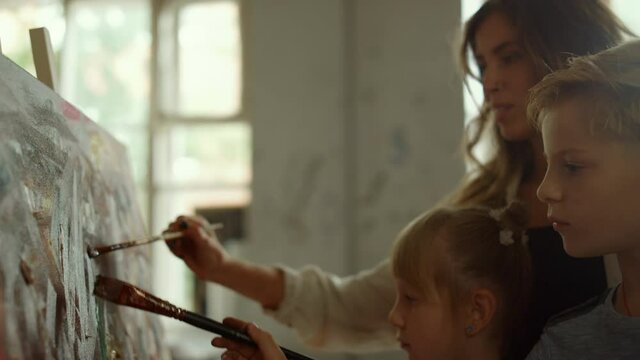 Female teacher and children drawing indoors. Family spending time in art studio.