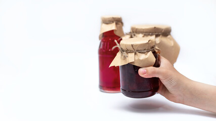 The hand holds another one, to Jars of different shapes with strawberry syrup and jam on a white...
