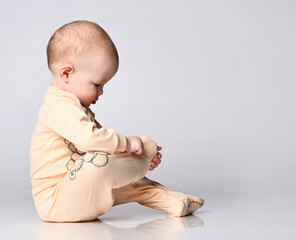 Little toddler Toddler child examines his leg with interest in a yellow cotton jumpsuit for toddlers.