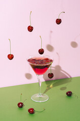 Abstact summer refreshment concept with cocktail glass with shadow and cherry fruit falling from above