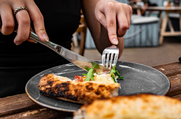 woman hands with knife and fork cutting pizza on table in cafe outdoor