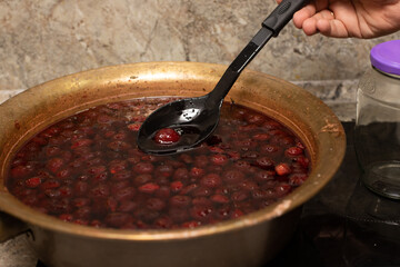 A man's hand holds a large spoon with strawberry jam on the background of Strawberry jam cooked in a copper basin.