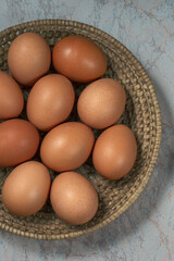 several fresh chicken eggs in a straw basket on a wooden background. Healthy eating concept.