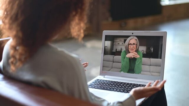 Grown daughter talk via video call on the laptop with a senior mother, lying on the couch and looks at the webcam. Two women differente generation have video meeting on the distance