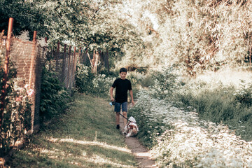 Teenage boy walks with dog on leash along the meadow