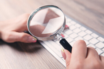 woman with a magnifying glass looks at the keyboard. online search