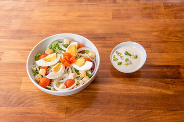 Bowl of homemade salad with boiled egg, croutons, mayonnaise with chives, lettuce, cherry tomatoes and raw white onion rings on wooden table