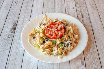 Caesar salad with lettuce, lots of mayonnaise, tomato and grated cheese sprinkled on a white plate