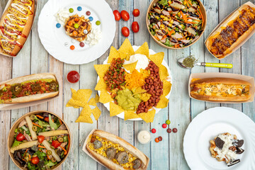 Foto top view de platos mexicanos, perritos calientes, ensaladas en bowl de servicio a domicilio y postes con lacasitos sobre fondo de madera