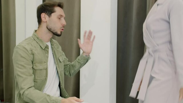 Portrait of unhappy guy grumping waiting for woman who is trying clothes in fitting room talking and gesturing complaining. Relationship and lifestyle concept.