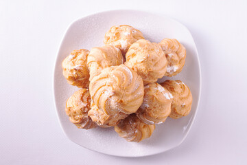 Profiteroles with cream on a white ceramic plate on a white background. Flat lay.