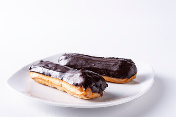 Eclairs with chocolate icing on a white plate.