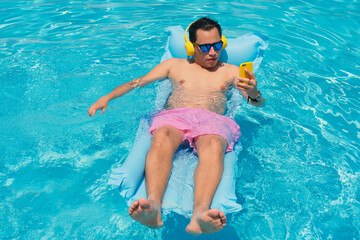 Hispanic Man sunbathing by the pool and holding cell phone in his hand