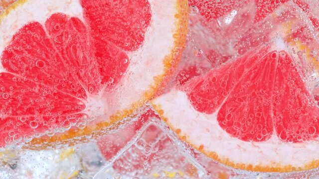 Super Slow Motion Shot of Fizzing Water with Grapefruit Slices and Ice Cubes in Glass at 1000 fps.