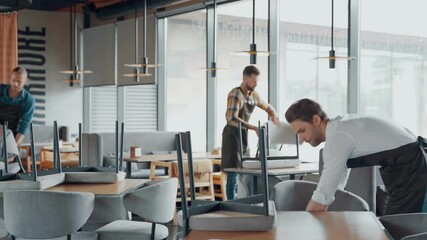 Male waiters in protective workwear arranging furniture in restaurant 